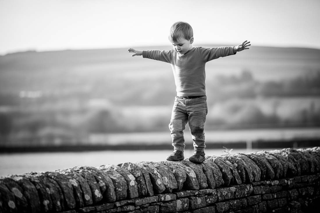A black and White Photo of a Young Boy Balancing On A Rock Wall