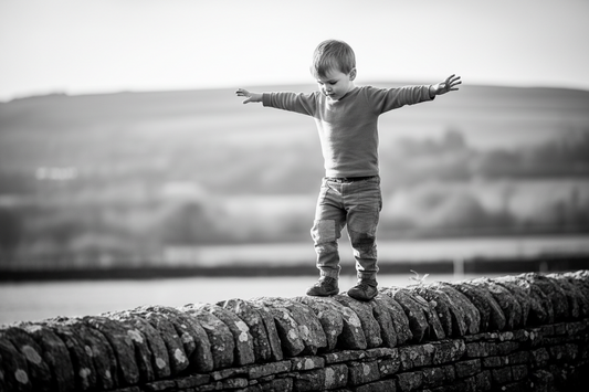 A black and White Photo of a Young Boy Balancing On A Rock Wall